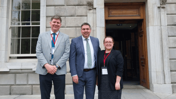 Three people dressed in formal business attire standing outside a stone building entrance, smiling for a photo.