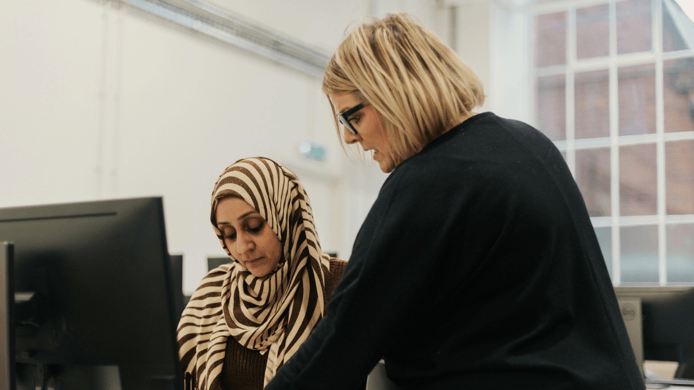 A trainer working through a technical exercise with a learner at a computer